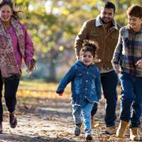 西班牙裔父亲和白人母亲在秋天带着他们的女儿和儿子在公园外面散步的照片